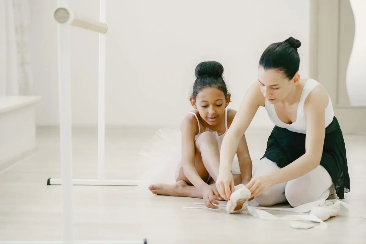 An instructor fitting a young ballet student's full-sole shoe.