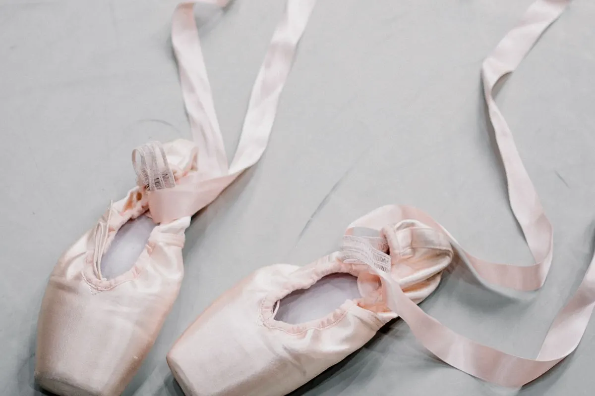 Pointe shoes and silk ribbons laid out on a studio floor.