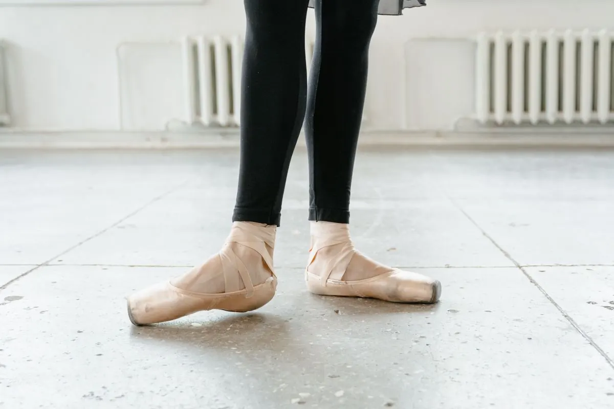 Ballet dancer in black leggings and pink split-sole ballet shoes.